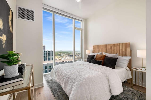 bedroom with visible vents, multiple windows, a wall of windows, and wood finished floors