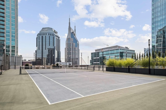 view of tennis court with community basketball court, fence, and a city view