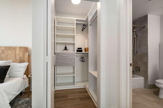 interior space with a spacious closet, toilet, wood finished floors, and tub / shower combination