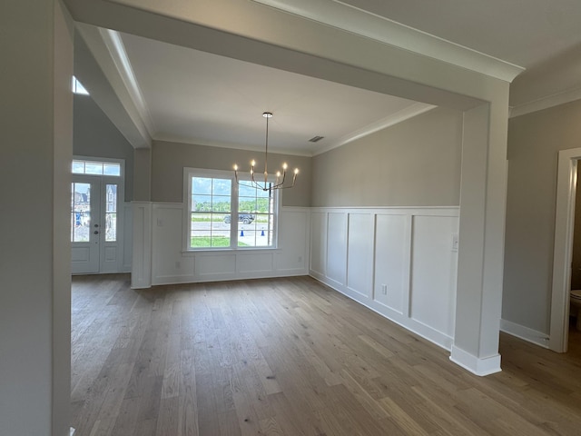 unfurnished dining area with an inviting chandelier, crown molding, a decorative wall, and wood finished floors