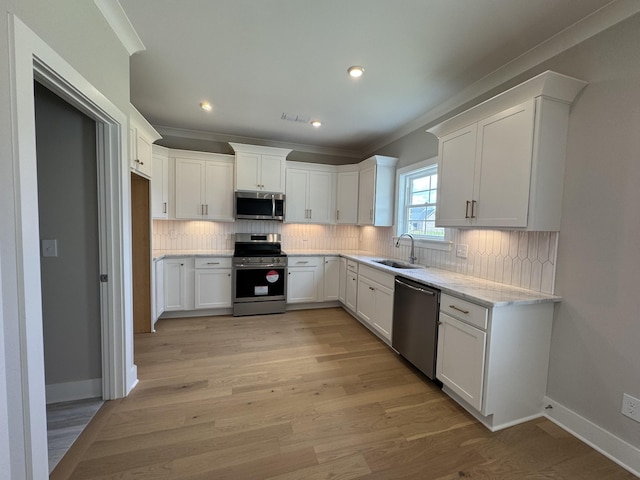 kitchen featuring crown molding, light wood-type flooring, white cabinets, a sink, and stainless steel appliances