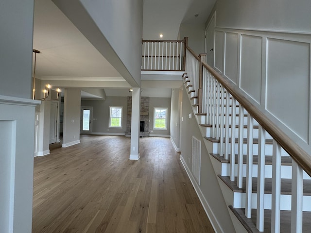 interior space featuring an inviting chandelier, a stone fireplace, baseboards, wood finished floors, and stairway