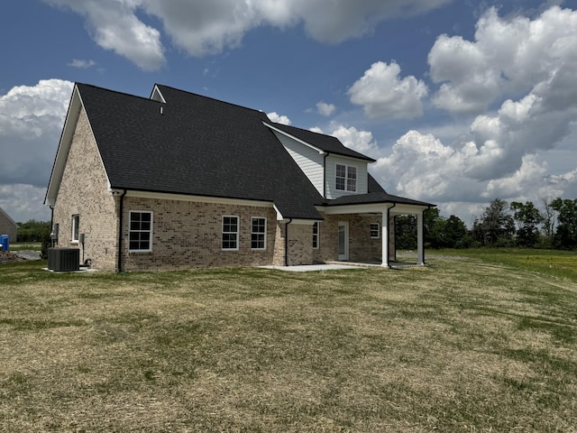 rear view of house with a yard, brick siding, cooling unit, and a shingled roof