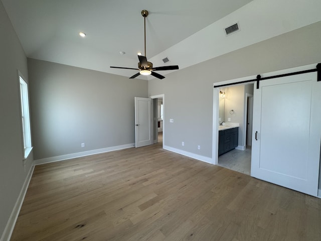 unfurnished bedroom featuring visible vents, light wood-style floors, baseboards, a barn door, and ensuite bath