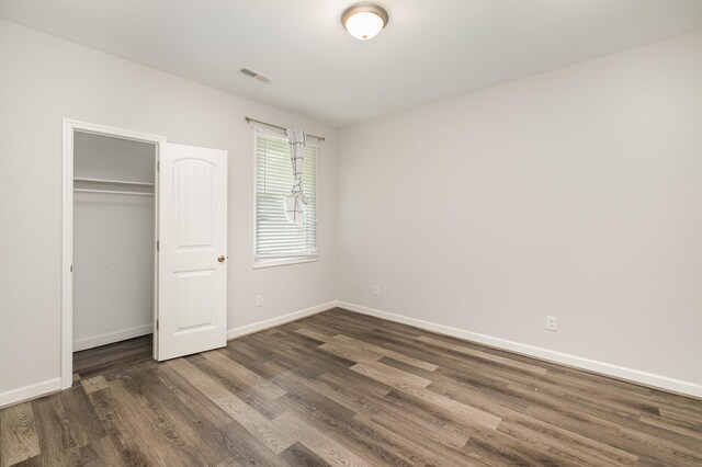 unfurnished bedroom with baseboards, a closet, wood finished floors, and visible vents