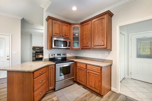 kitchen featuring brown cabinetry, crown molding, light stone counters, a peninsula, and stainless steel appliances