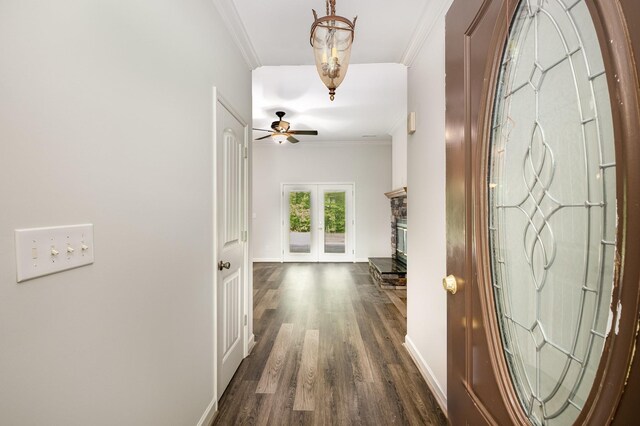 foyer entrance with ornamental molding, a fireplace, baseboards, a ceiling fan, and dark wood finished floors