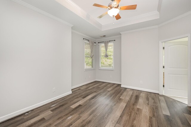 empty room with crown molding, dark wood-style flooring, a raised ceiling, a ceiling fan, and baseboards