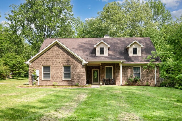 cape cod home with brick siding, a chimney, and a front yard