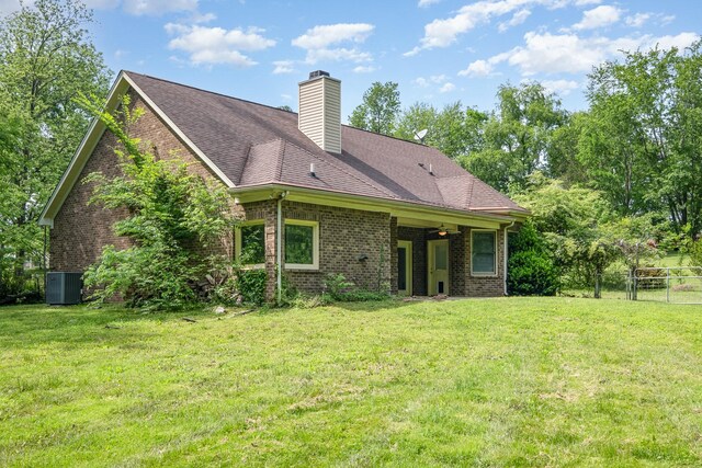 rear view of property with fence, brick siding, a chimney, cooling unit, and a yard