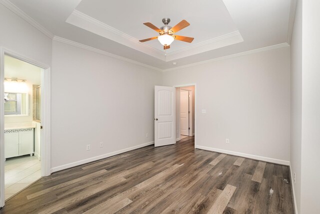 unfurnished room with ceiling fan, wood finished floors, baseboards, ornamental molding, and a tray ceiling