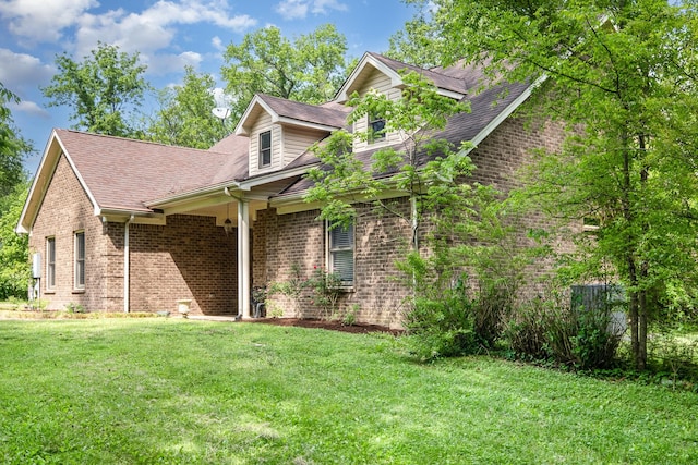 exterior space with a shingled roof, a yard, and brick siding
