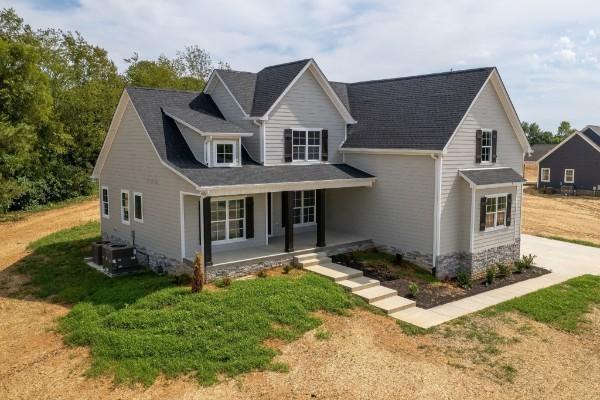 traditional-style home with a front lawn, an attached garage, central AC, concrete driveway, and a porch