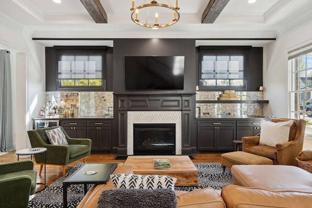 living area with wood finished floors, beamed ceiling, a chandelier, ornamental molding, and coffered ceiling