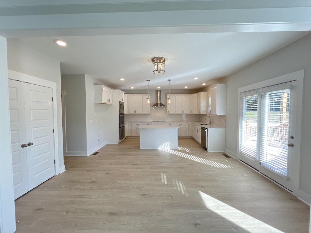 kitchen featuring wall chimney range hood, a sink, dishwasher, backsplash, and a kitchen island