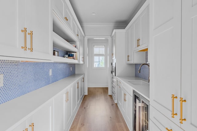 kitchen featuring decorative backsplash, a sink, light countertops, white cabinets, and beverage cooler