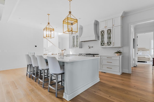 kitchen with light wood-style floors, a sink, custom exhaust hood, and tasteful backsplash