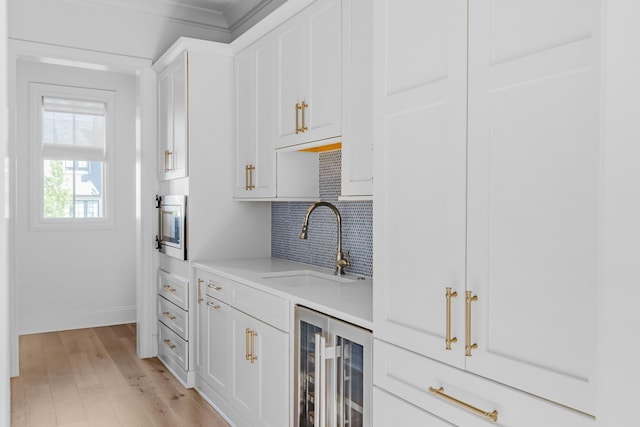 kitchen with backsplash, a sink, light countertops, beverage cooler, and light wood-style floors