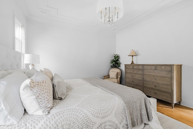 bedroom with a chandelier, ornamental molding, wood finished floors, and a raised ceiling