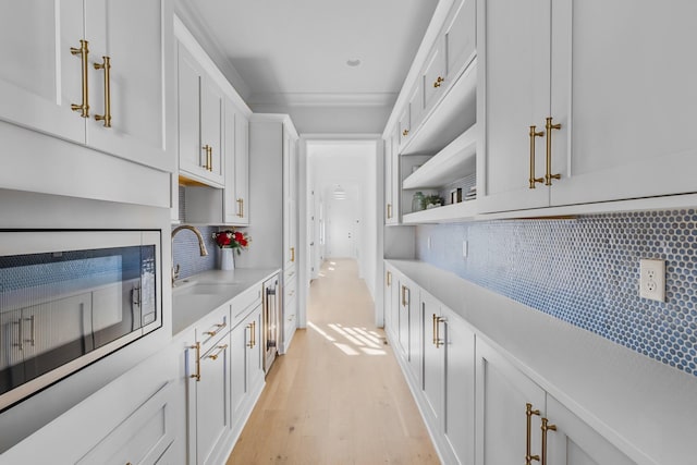 kitchen with light countertops, built in microwave, tasteful backsplash, a sink, and light wood finished floors