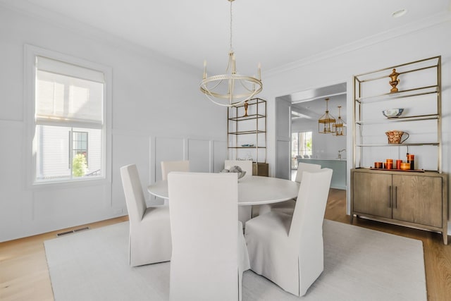 dining area featuring visible vents, ornamental molding, a wainscoted wall, a chandelier, and light wood-style flooring