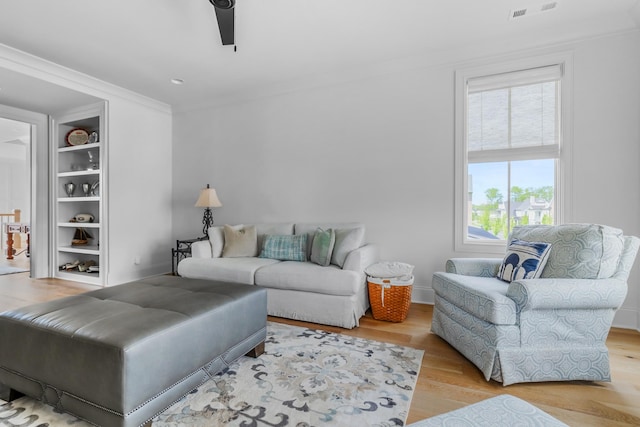 living room with visible vents, crown molding, built in features, wood finished floors, and a ceiling fan