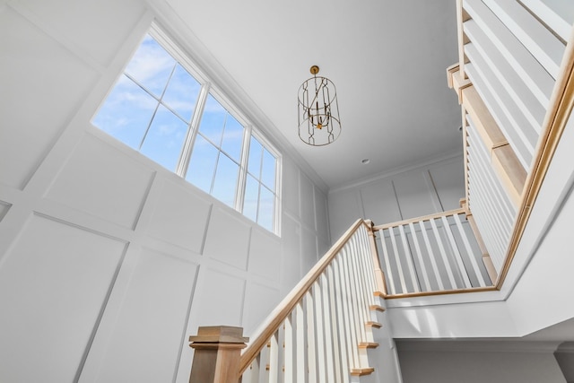stairway featuring an inviting chandelier, a towering ceiling, and a decorative wall