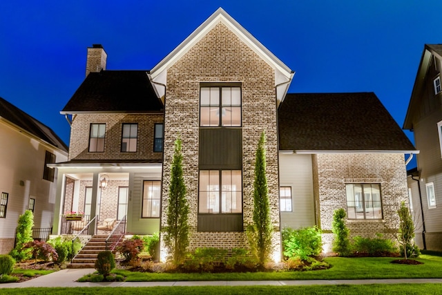 exterior space featuring a porch, brick siding, a yard, and a chimney