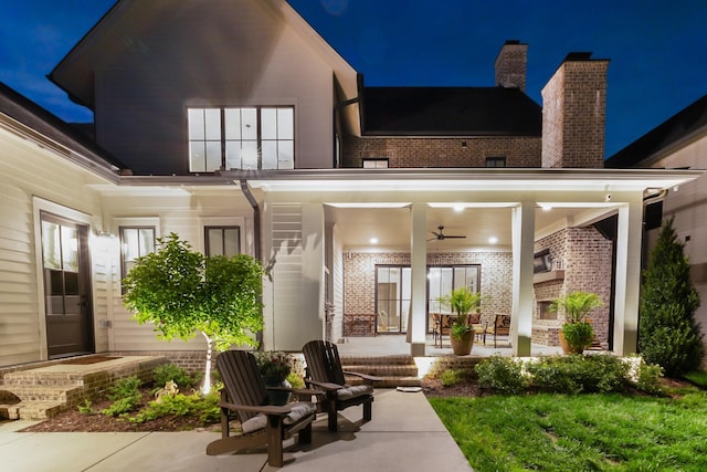exterior space featuring brick siding, ceiling fan, a chimney, and a patio