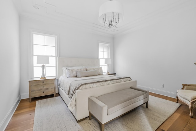 bedroom featuring baseboards, ornamental molding, light wood finished floors, and a notable chandelier