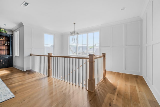hall featuring a notable chandelier, light wood finished floors, a decorative wall, an upstairs landing, and visible vents