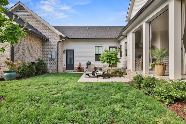 back of property with a lawn, a patio, roof with shingles, and brick siding