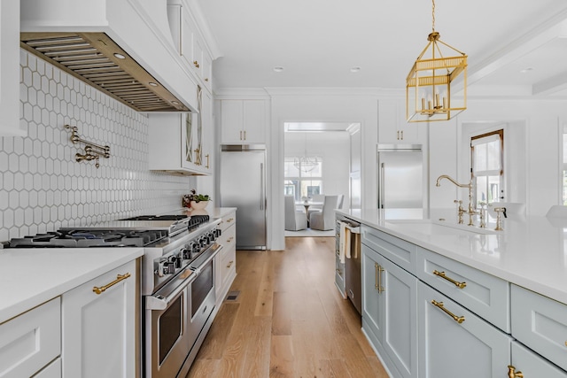 kitchen with a sink, high end appliances, an inviting chandelier, and custom exhaust hood