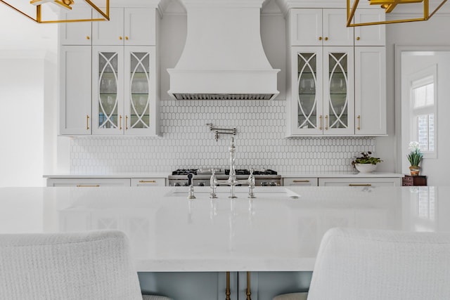 kitchen with light countertops, custom exhaust hood, glass insert cabinets, and tasteful backsplash