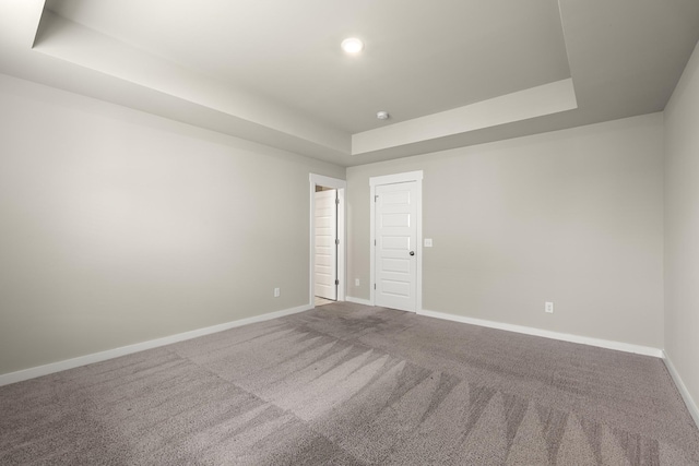 empty room with carpet flooring, a tray ceiling, and baseboards