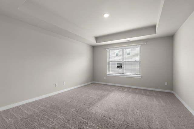 spare room with carpet floors, a tray ceiling, and baseboards