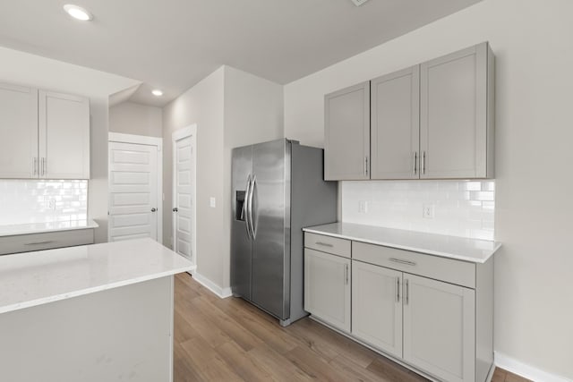 kitchen with baseboards, light wood-style floors, stainless steel fridge, gray cabinets, and backsplash