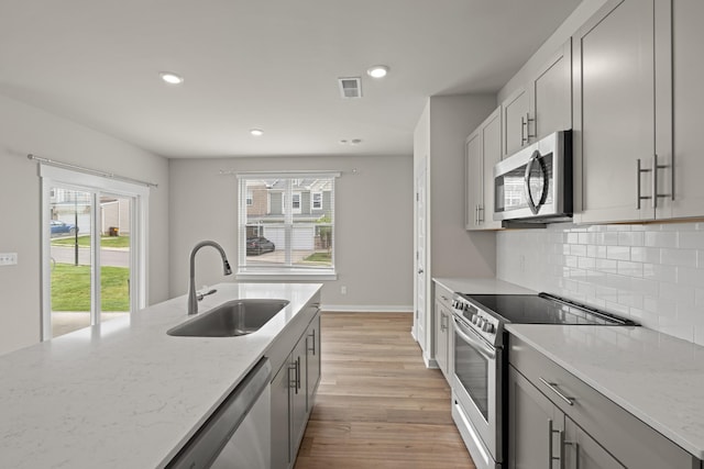kitchen featuring decorative backsplash, appliances with stainless steel finishes, light stone countertops, a sink, and light wood-style flooring