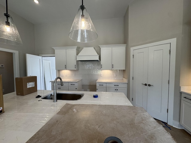 kitchen featuring decorative backsplash, decorative light fixtures, a sink, premium range hood, and white cabinetry