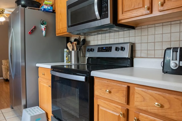 kitchen featuring light countertops, brown cabinetry, stainless steel appliances, light tile patterned floors, and backsplash