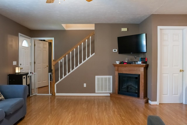living area featuring visible vents, wood finished floors, baseboards, a glass covered fireplace, and stairs