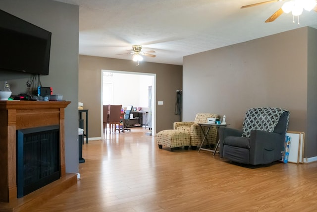 living area with ceiling fan, a fireplace, and light wood finished floors