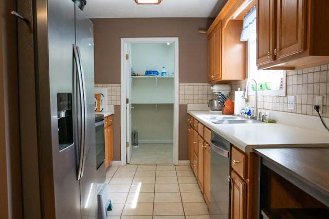 kitchen featuring light tile patterned flooring, brown cabinets, a sink, backsplash, and stainless steel appliances
