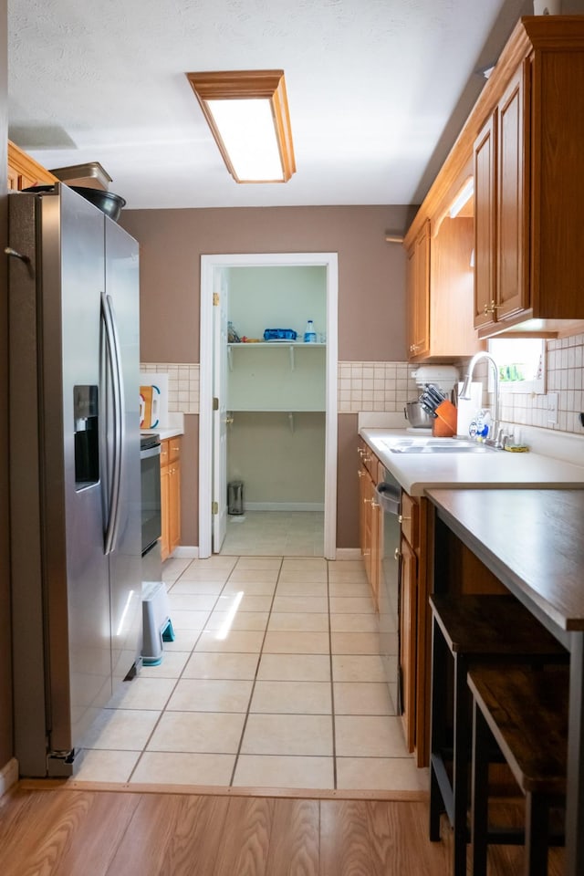 kitchen with a sink, appliances with stainless steel finishes, brown cabinetry, and backsplash