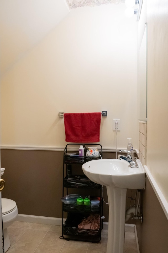 half bathroom with tile patterned floors, baseboards, toilet, and lofted ceiling