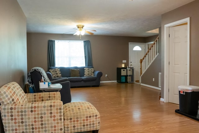 living room with stairway, baseboards, a ceiling fan, and light wood finished floors