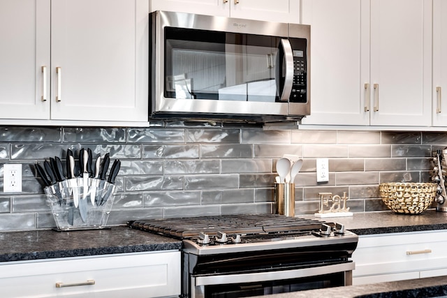 kitchen with white cabinets, stainless steel appliances, dark countertops, and tasteful backsplash