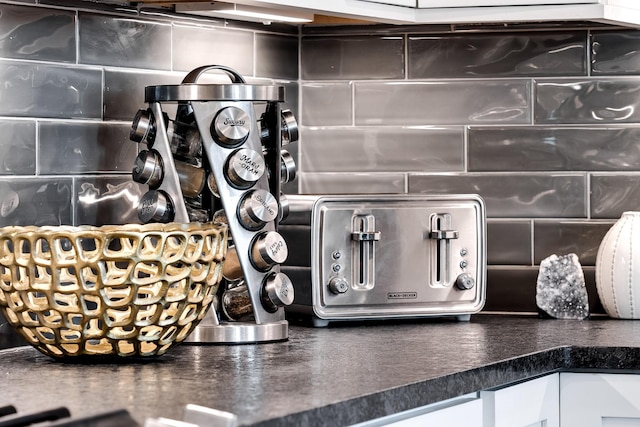 interior details with decorative backsplash, white cabinets, and dark countertops