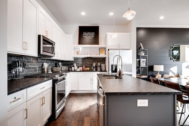 kitchen featuring dark countertops, appliances with stainless steel finishes, a sink, a kitchen island with sink, and dark wood-style floors