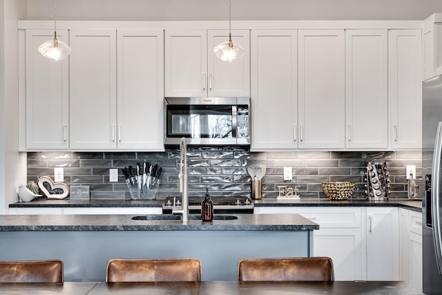 kitchen with white cabinetry, stainless steel microwave, backsplash, and decorative light fixtures